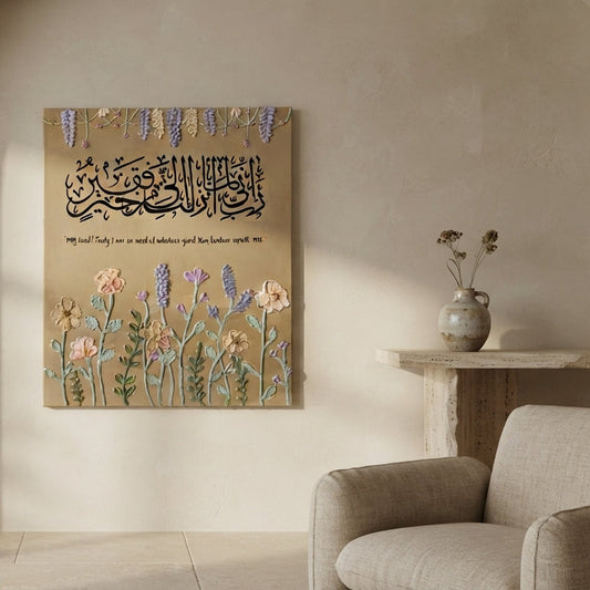 A square wall art print featuring Arabic calligraphy and floral illustrations in soft pastel tones, displayed on a beige wall in a styled interior with a sofa and side table.